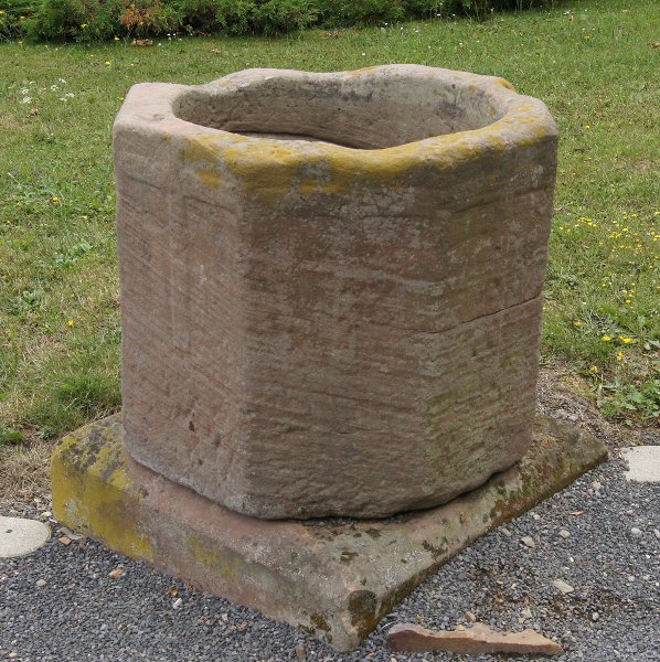 Ein alter Taufstein unbekannter Herkunft, der zur Zeit einen Platz vor der Kirche gefunden hat